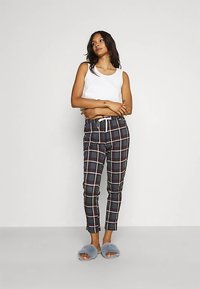 White tank top, black and red plaid trousers with white accents, fitted design, and gray fuzzy slippers. Smooth fabric and comfortable fit.