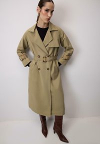 Bež plašč z dvojnim zapenjanjem in pasom, z velikimi klapnicami in gumbnimi manšetami. Obut nad črnim zgornjim delom, dopolnjen s rjavimi škornji s koničastim nosom.