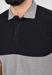 Rövid ujjú polo póló fekete felső résszel és szürke alsó résszel. Szürke gallérral, négy fekete gombbal és texturált anyagmintázattal rendelkezik.