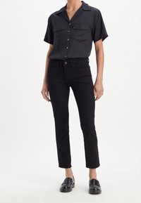 Svart kortärmad skjorta med knappar och två bröstfickor, kombinerad med svarta slim-fit jeans och svarta loafers. Slät tyg, skräddarsydd design.