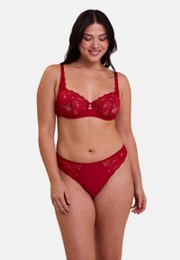 Un soutien-gorge en dentelle rouge et un string assorti présentent des motifs floraux, des bonnets semi-transparents et une ceinture lisse. Le tissu est doux avec des détails délicats.