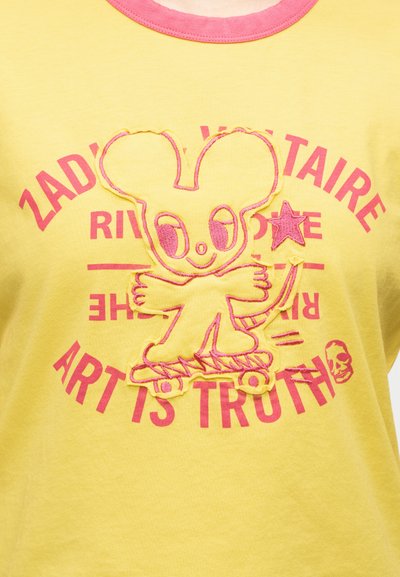 Κίτρινη μπλούζα με ροζ γιακά που απεικονίζει έναν καρτούν ποντικό πάνω σε σκέιτμπορντ κρατώντας ένα αστέρι, περιτριγυρισμένο από ροζ κείμενο που λέει "Η ΤΕΧΝΗ ΕΙΝΑΙ ΑΛΗΘΕΙΑ."