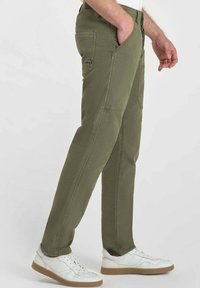 Pantalons vert olive à coupe droite, dotés de multiples poches et de coutures contrastées, associés à des baskets blanches.