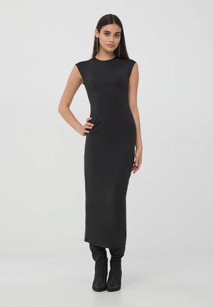 Abito maxi nero, senza maniche, aderente al corpo, con un collo alto. Tessuto liscio con una leggera lucentezza, abbinato a stivali neri alti e testurizzati.