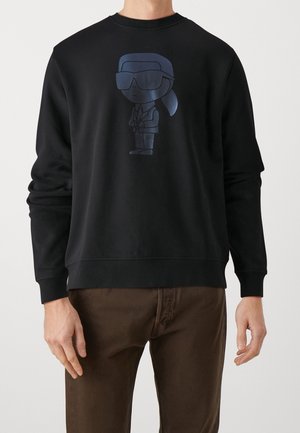 Sweatshirt noir avec un graphique brillant d'un personnage de dessin animé en costume et lunettes de soleil à l'avant. Tissu doux avec une coupe décontractée.