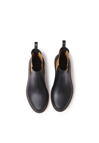 Bottes de cheville en caoutchouc noir avec une finition lisse, doublure intérieure tan contrastante et couture jaune le long de la semelle. Poignées à l'arrière.