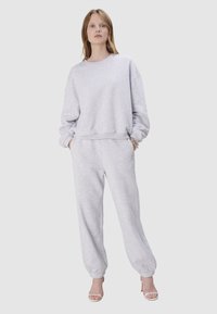Sweat-shirt gris et pantalon de jogging assorti en tissu doux. Le sweat-shirt a un col rond ; le pantalon a des poignets élastiques et des poches latérales.