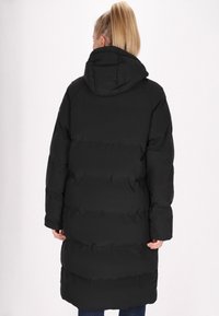 Parka nera con cappuccio, design lungo, motivo trapuntato e maniche ampie. Il materiale sembra liscio e isolato per garantire calore.