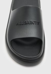 Sandale negre cu talpă plată, fabricate dintr-un material sintetic neted, având o curea lată gravată cu numele mărcii "ALLSAINTS" în litere mari.