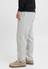 Grijze sweatpants met elastische tailleband, zijzakken en een relaxte pasvorm, gecombineerd met bruine casual schoenen. Zachte stoftextuur.
