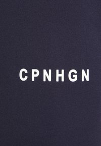 Tela de color marino con textura acanalada presenta las letras blancas "CPNHGN" prominentemente centradas. El diseño es minimalista y moderno.