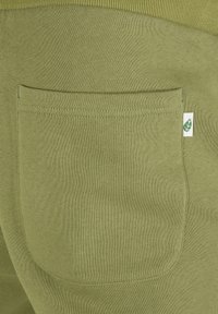 Olivgrüne Stoffshorts mit einer hinteren Aufsatztasche und einem kleinen Blatt-Logo. Das Material ist glatt und hat eine weiche Textur.