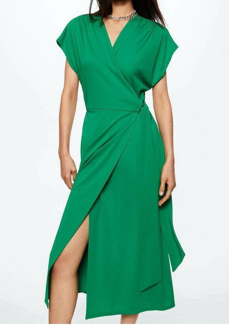 Mujer vestida con un vestido envolvente verde con escote en V, mangas cortas, abertura lateral y un lazo en la cintura, complementado con un collar de cadena plateado.