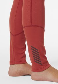 Leggings deportivos rojos con tejido texturizado, diseño ajustado y costuras en tono. Presentan un gráfico de rayas negras en la parte inferior de la pierna.