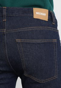 Tmavě modré džíny z denimu s koženou nášivkou "WEEKDAY" na pasu, se standardním šitím a zadními kapsami.