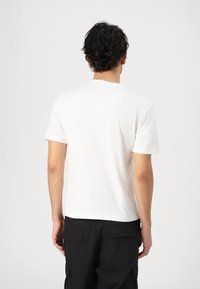 T-shirt bianca in cotone con scollatura tonda e maniche corte, caratterizzata da un design semplice senza motivi o accenti. Pantaloni cargo neri visibili.