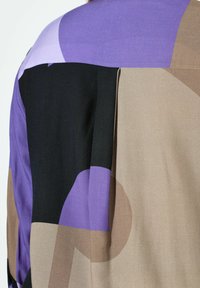 Multikleurenblouse met een geometrisch patroon. Heeft paarse, zwarte en beige delen met een gladde textuur en een losse pasvorm.