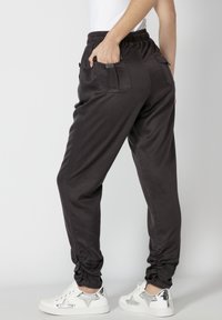 Pantalons de jogging gris foncé avec une taille élastique, des poches latérales et des poignets froncés, associés à des baskets blanches avec des accents argentés.