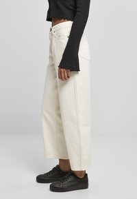 Breda jeans i krämfärg gjort av slitstark tyg, med hög midja, framfickor och ihopparad med svarta snörskor.