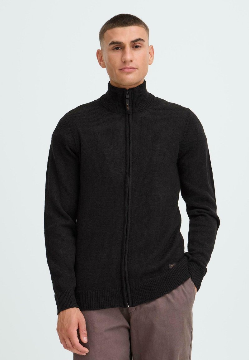Svart zip-up tröja med hög krage, ribbade ärmslut och nederkant. Tillverkad av strukturerad tyg, med en logotypdetalj på sidan.
