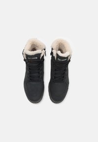 Svarte høyre boots med teksturert yttermateriale, myk krave i kremfarge, og snøresystem, med gummisåler og merket detalj.