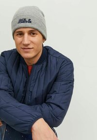 Giubbotto bomber trapuntato blu navy con zip e polsini a costine, abbinato a un berretto lavorato a maglia grigio chiaro con un logo blu scuro.