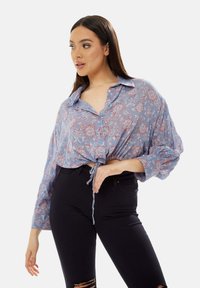 Light blue cropped blouse featuring a floral pattern in red and white, button-down front, and tie detail at the waist. Soft, lightweight fabric.