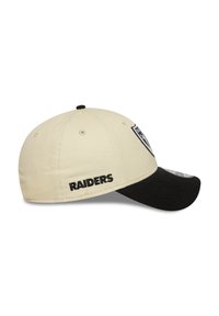 Boné de basebol bege com a aba preta. Apresenta "RAIDERS" bordado em preto. Patch do logo na parte frontal. Forma ligeiramente arredondada.