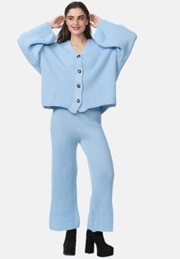 Ensemble tricoté deux pièces bleu clair comprenant un cardigan cropped à boutons avec de gros boutons et des manches larges, assorti à un pantalon ajusté en côte.