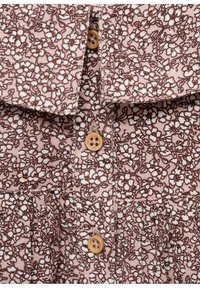Smeđi tkanina s cvjetnim uzorkom na ružičastoj pozadini, s ovratnikom i drvenim gumbima, ističući teksturirani, slojeviti dizajn.