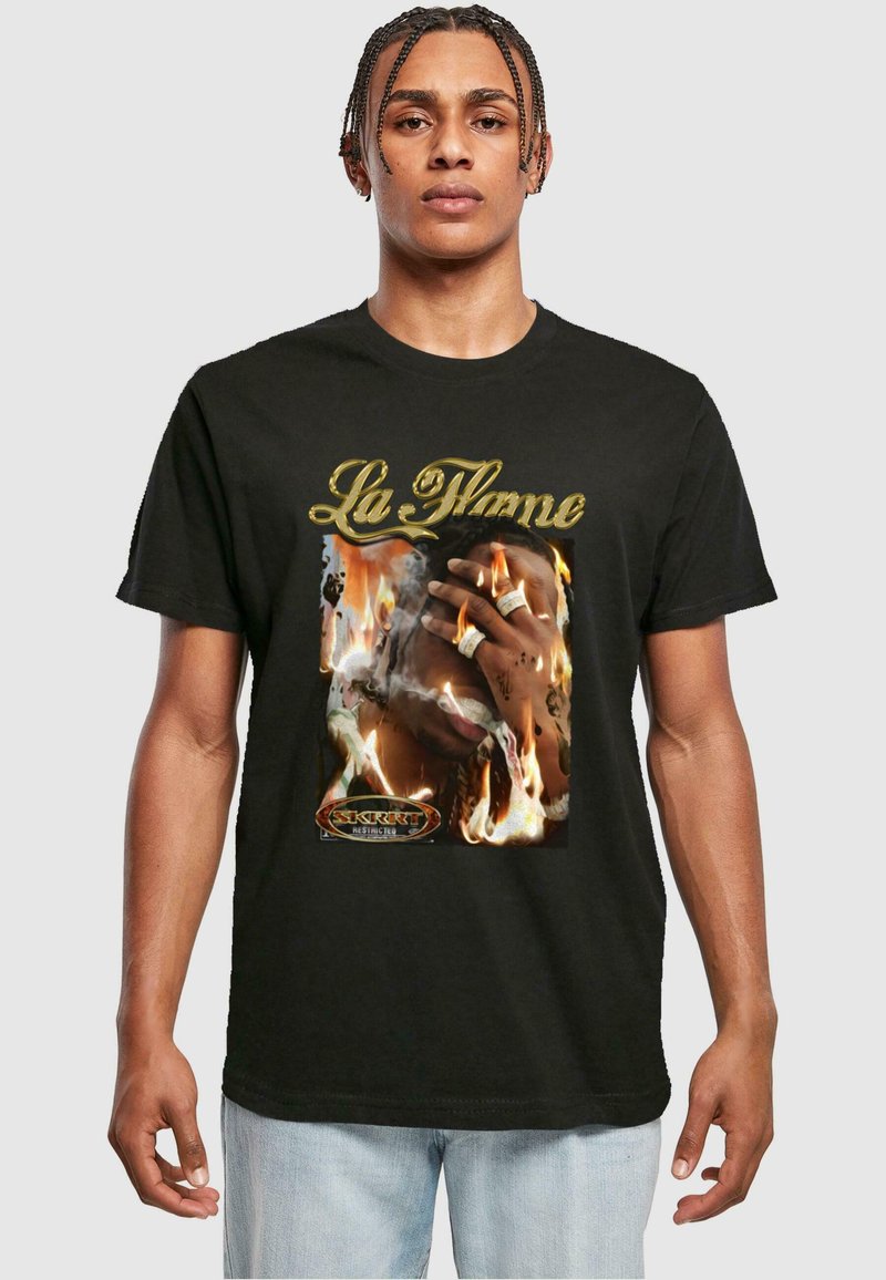 Melna kokvilnas T-kreklu ar grafisku attēlu, kurā redzama roka ar gredzeniem pret uguns fonu; teksta "La Flame" zeltā virs un logotips apakšā.