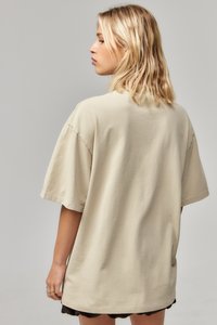 Beige oversized t-shirt met korte mouwen, casual ontwerp, zachte textuur en een rechte zoom, gedragen over een zwarte gelaagde rok.