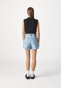 Čierny bezrukávový top, svetlomodré denímové šortky s strapcami, strieborné detaily a čierne topánky s bielymi ponožkami. Čisté, minimalistické pozadie.