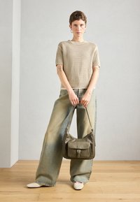 Top tricoté beige à manches courtes, jeans larges en denim clair, et un sac à bandoulière en cuir vert foncé. Ballerines blanches à bout pointu.