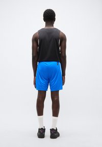 Αθλητική στολή που περιλαμβάνει μαύρο αμάνικο τοπ και μπλε σορτς, συνδυασμένη με μαύρα αθλητικά παπούτσια με πολύχρωμες λεπτομέρειες και λευκές κάλτσες.