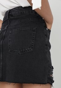 Zwarte denim minirok met een hoge taille, rafelrand en een achterzak, met een klassieke snit en gestructureerde stof.