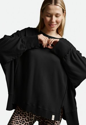 Schwarzer übergroßer Sweatshirt mit gerippten Bündchen und seitlichen Schlitzen, kombiniert mit Leggings im Tiermotiv. Weicher Stoff, lockere Passform, minimale Markenkennzeichnung.