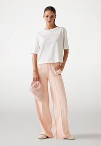 T-shirt bianco corto con logo "GUESS", abbinato a pantaloni palazzo rosa pallido e un cappello abbinato. Tessuto morbido con vestibilità casual.