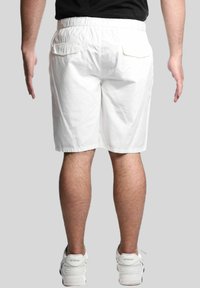 Corto in cotone bianco con una vestibilità rilassata, dotato di una vita elasticizzata e due tasche posteriori, abbinati a sneakers sportive bianche.