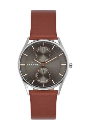 Reloj de pulsera Skagen con correa de cuero marrón, esfera gris, caja plateada, subesferas de día y fecha, y marcadores y agujas de hora delgadas en tono dorado.