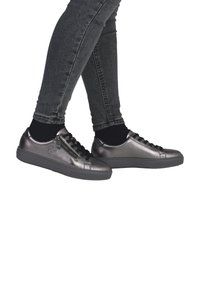 Sneaker metallic grigie con lacci neri e una cerniera laterale, progettate con una suola in gomma testurizzata e una punta rotonda. Indossate con calzini neri alla caviglia.