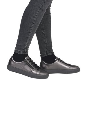 Baskets gris métallique avec des lacets noirs et une fermeture éclair sur le côté, conçues avec une semelle en caoutchouc texturé et un bout rond. Portées avec des chaussettes noires à la cheville.