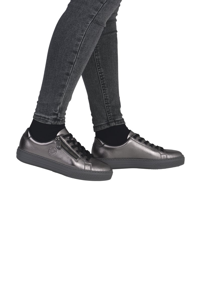 Sneaker metallic grigie con lacci neri e una cerniera laterale, progettate con una suola in gomma testurizzata e una punta rotonda. Indossate con calzini neri alla caviglia.