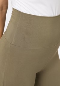Legíny vysokého pasu v olivově zelené barvě, vyrobené z pružné látky s hladkou strukturou a bezšvým designem. Obsahují nenápadný pas.