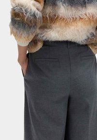 Pantalones de lana gris con un corte entallado, que cuentan con dos bolsillos traseros. La modelo lleva un suéter esponjoso y multicolor con un diseño texturizado.