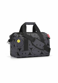 Borsa a secchio grigia con motivi a faccina sorridente nera, manici neri e tracolla, e un ciondolo a forma di faccina sorridente gialla sul cursore della zip.