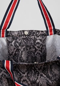 Zwarte en grijze gedrukte draagtas met een reptielenhuidpatroon, voorzien van rood en marineblauwe gestreepte handvatten en een drukknoopsluiting. Interne tas zichtbaar.