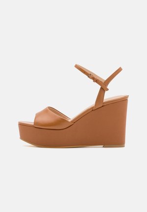 Sandales compensées en cuir marron avec un design large et ouvert à l'avant, une sangle réglable à la cheville et un talon compensé texturé pour plus de stabilité.