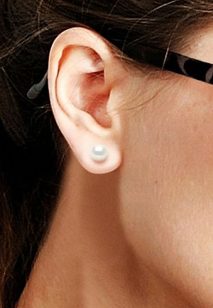 Boucle d'oreille en perle blanche ronde dans une oreille percée. Texture lisse, finition brillante. Vue rapprochée montrant le détail du lobe et du sertissage de la boucle d'oreille.