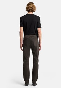 Schwarzes T-Shirt mit kurzen Ärmeln, kombiniert mit dunkelbraunen Hosen; verfügt über ein gerades Bein-Design, sichtbare Nähte und zwei Gesäßtaschen.